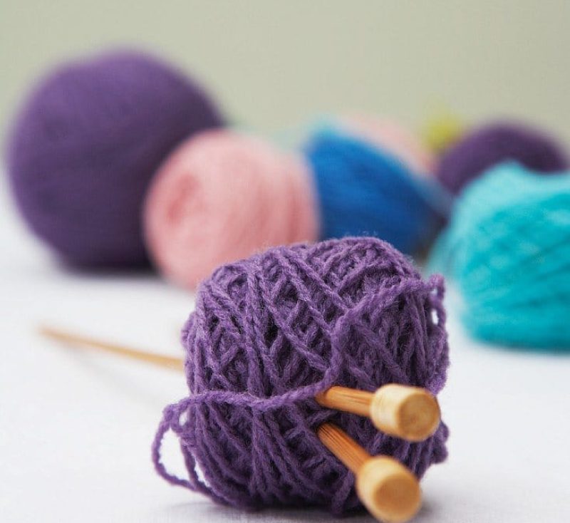 Mehrere Wollknäuel, eines mit Stricknadeln